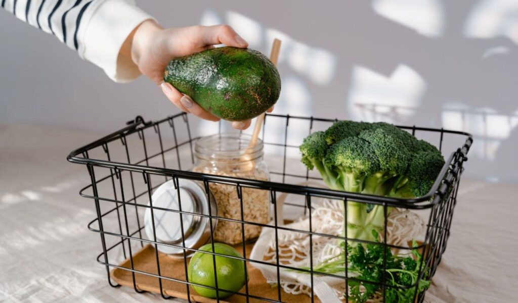 A Person Holding Green Avocado Above a Black Steel Basket