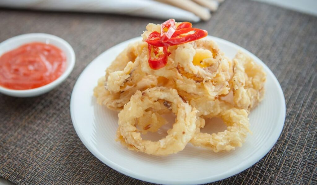 A white plate topped with onion rings next to a bowl of ketchup