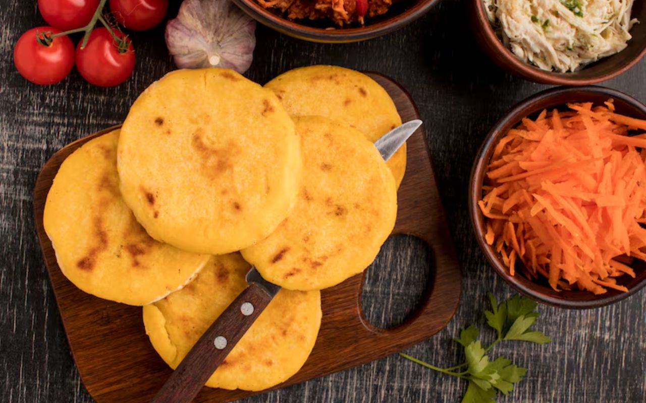 Arepas on a wooden board with grated carrots and other sides