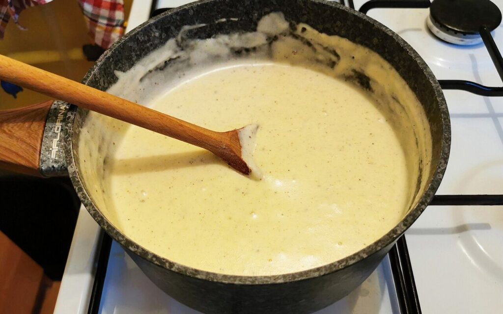Wooden spoon stirring creamy béchamel sauce in a pot on a stove