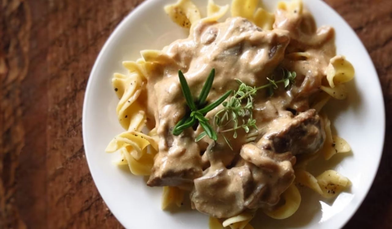Beef stroganoff served over egg noodles, garnished with fresh herbs