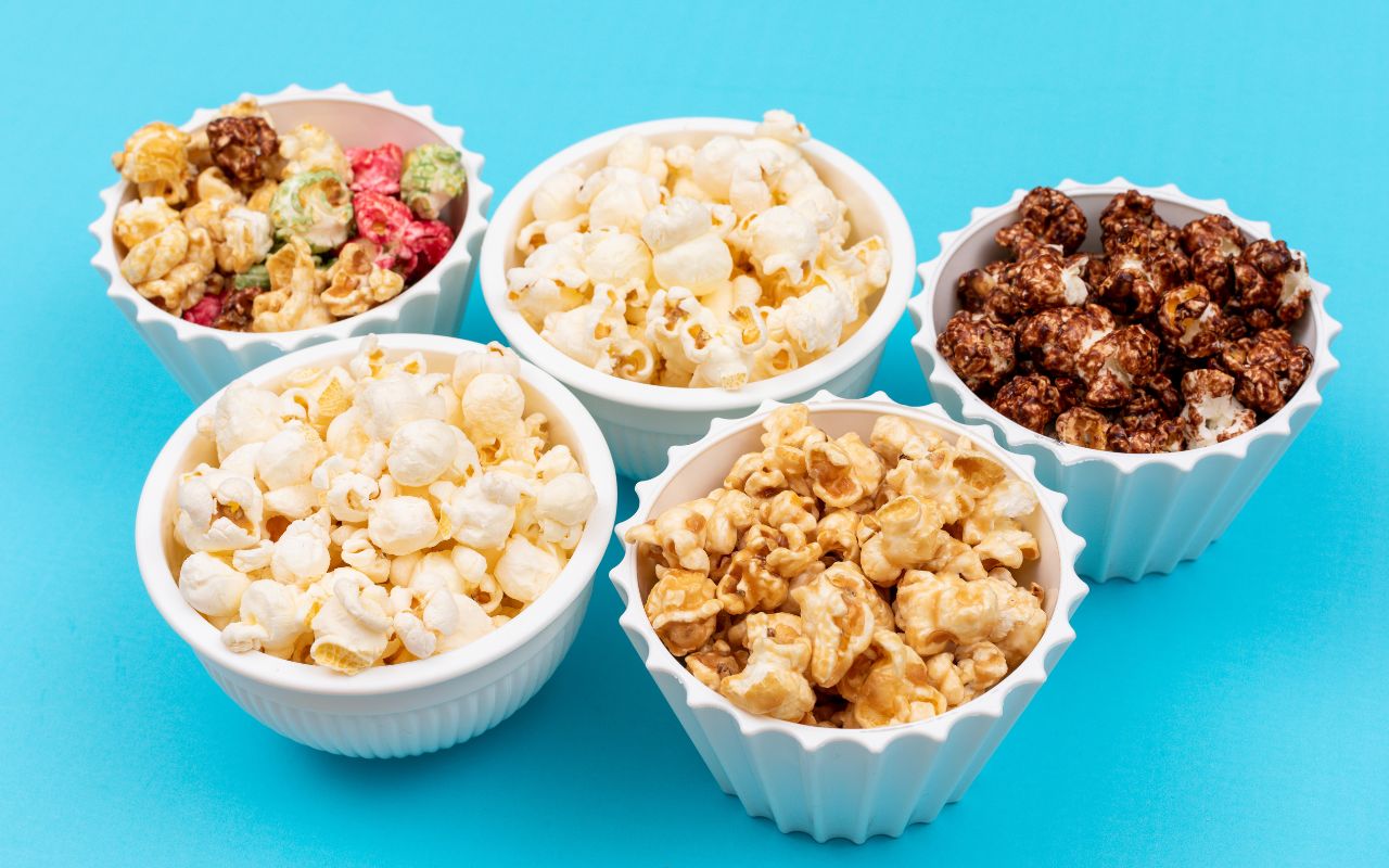 Assorted flavored popcorn in white bowls on blue background