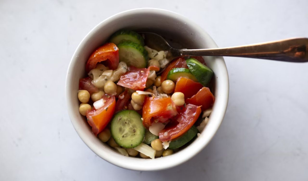 Garbanzo bean, cucumber, tomato salad in bowl with copper colored spoon