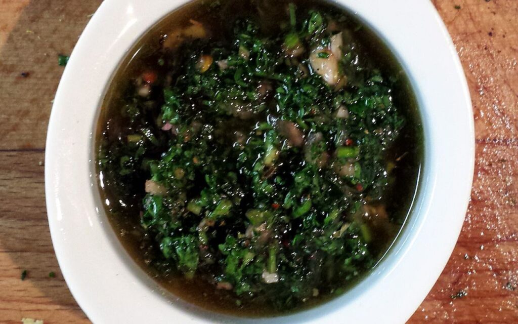 A bowl of chimichurri sauce with chopped herbs and oil