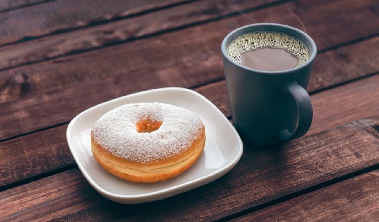 Doughnut on white ceramic plate beside mug of coffee
