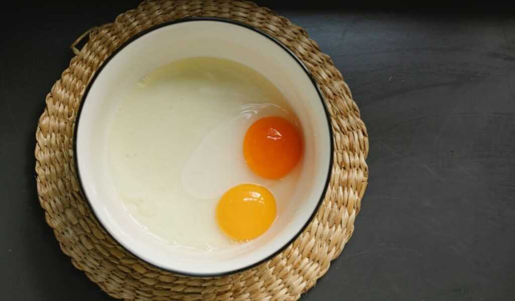 Uncooked broken eggs in bowl placed on wicker table mat