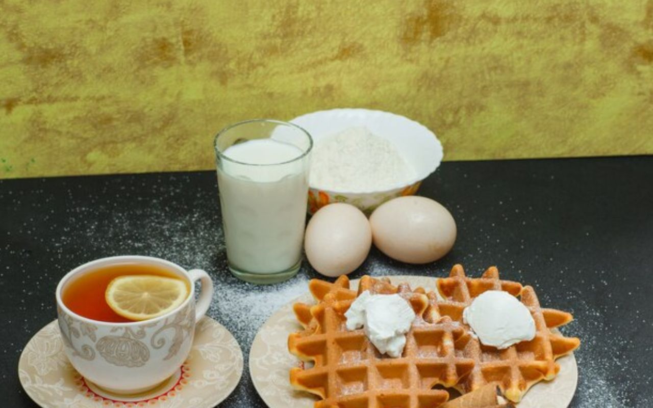 Waffles with cream served alongside tea, milk, and baking ingredients