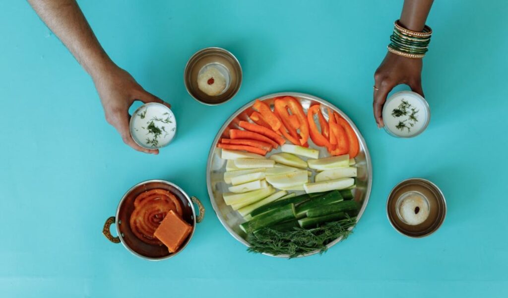 Hands holding cup of dip next to plate of cut vegetables