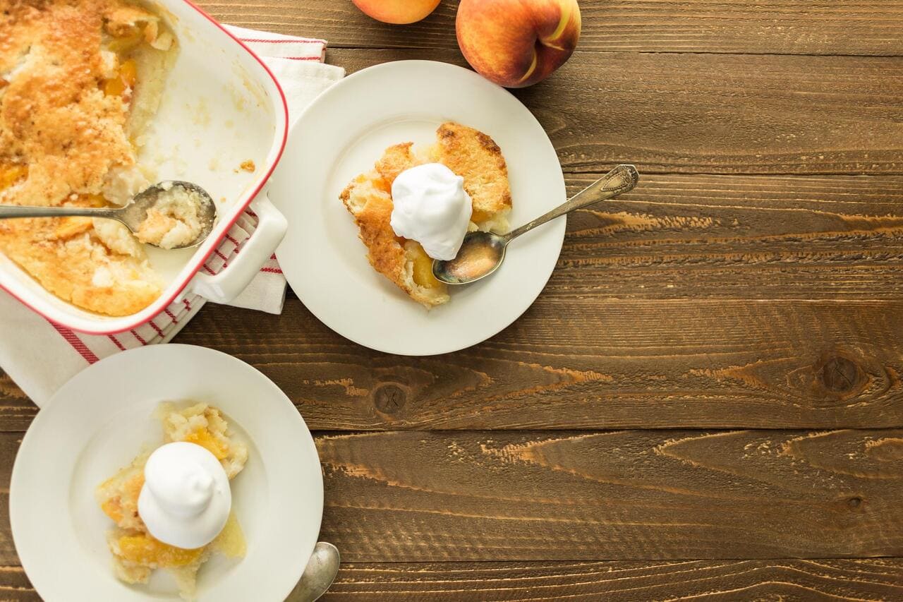 Freshly baked peach cobbler with scoop of whipped cream.