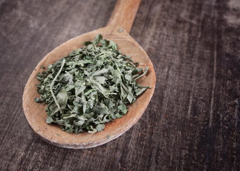 chopped dried parsley in wooden spoon on plank