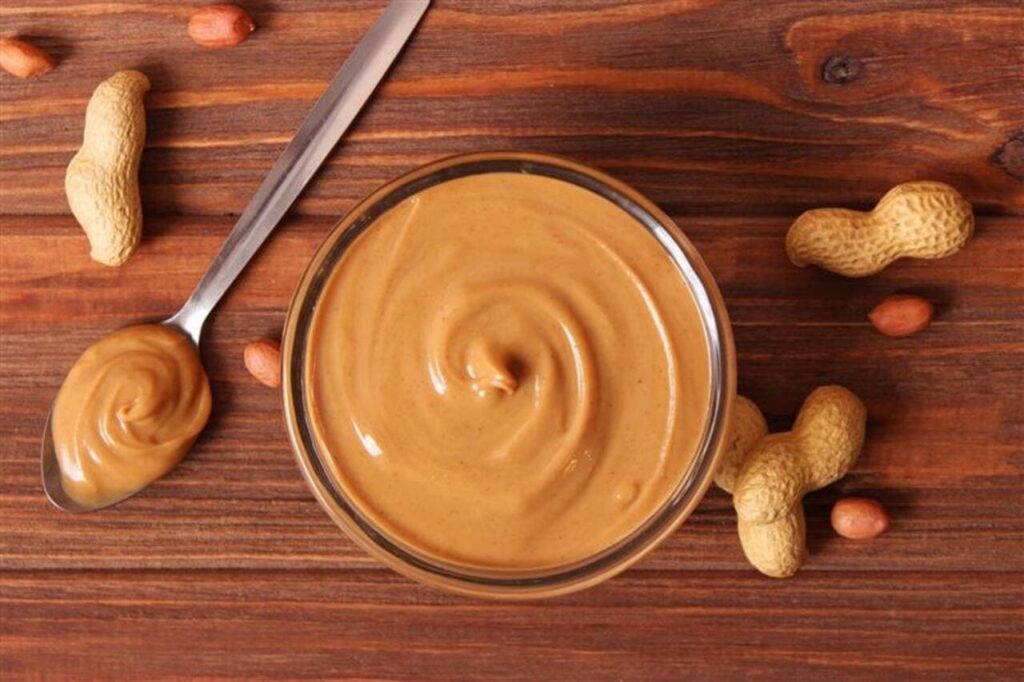 creamy peanut butter and peanuts beans on wooden background top view