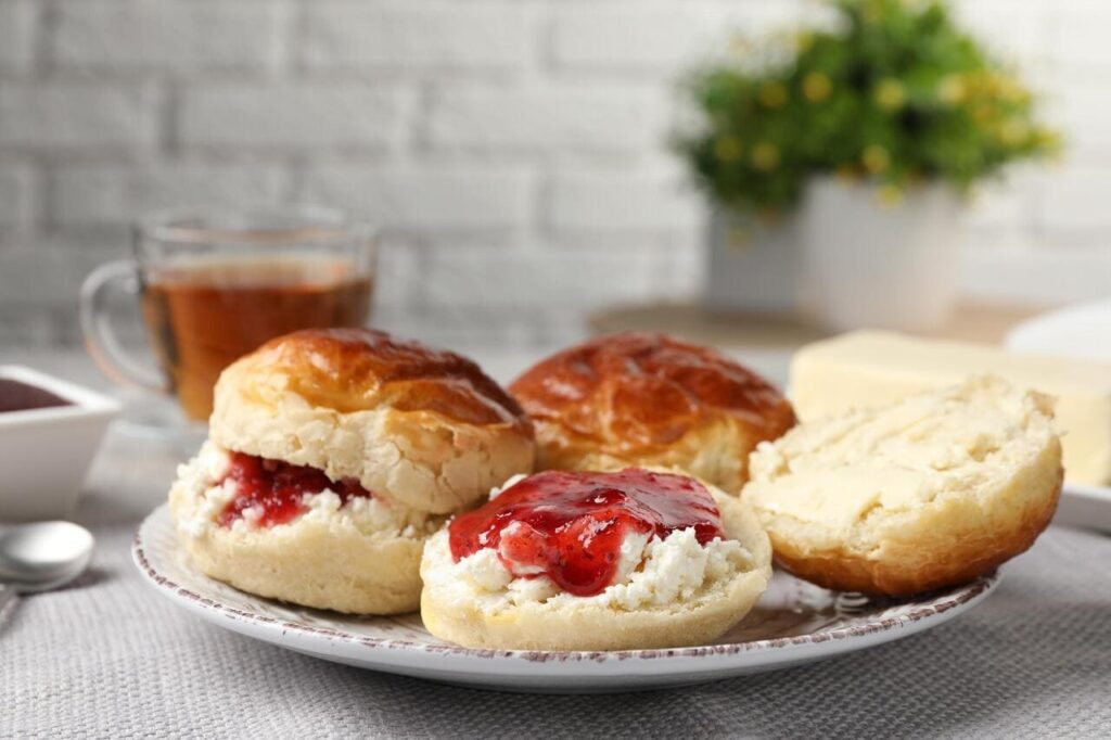 Freshly baked soda water scones with cranberry jam and butter on light gray mat, closeup