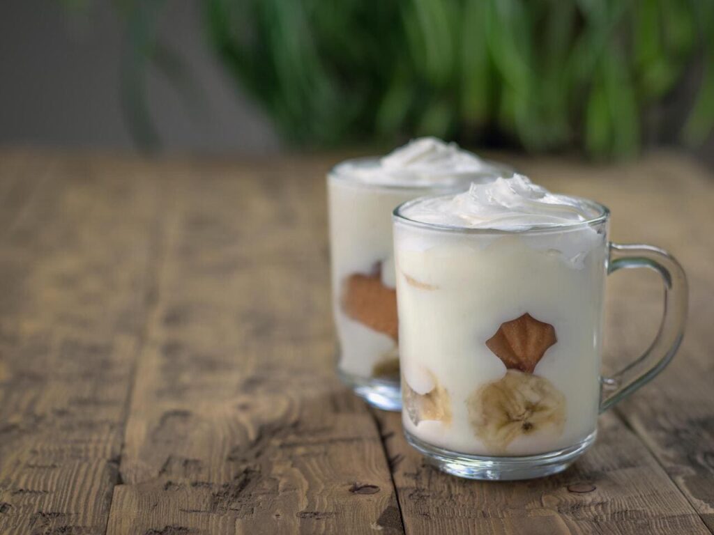 Banana pudding with cookies decorated with whipped cream on a wooden table.