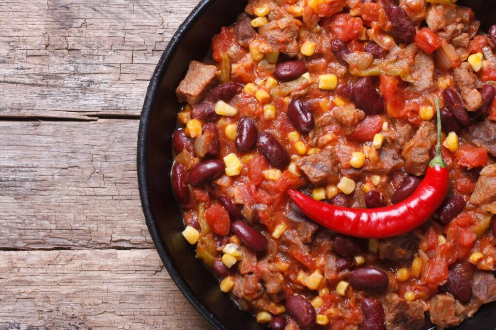 chili con carne close-up in a frying pan on a wooden background. horizontal top view