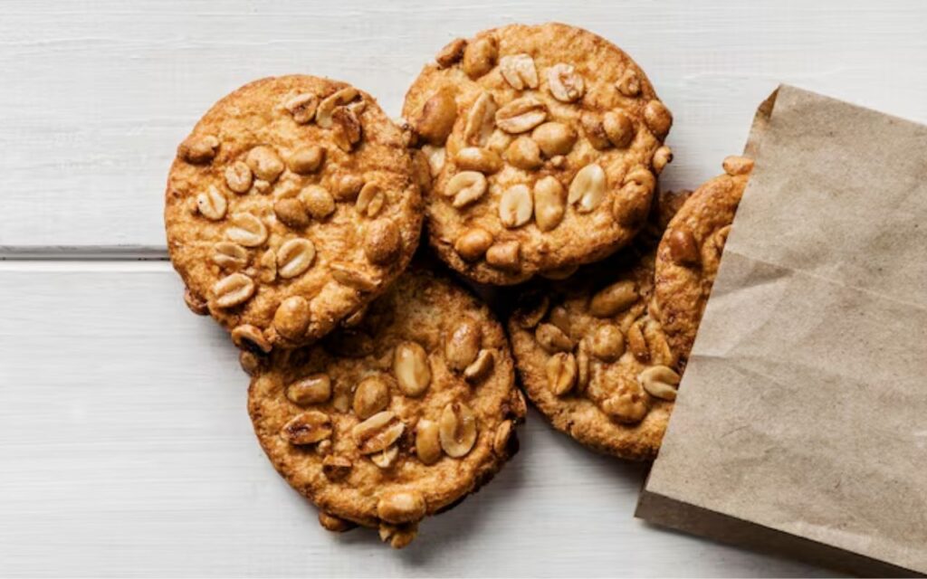 Peanut butter cookies with peanuts on top, arranged next to a brown paper bag