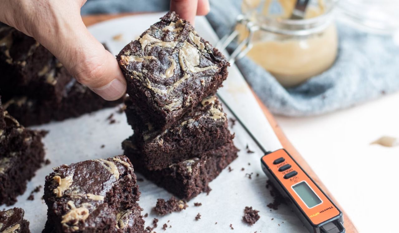 Person holding chocolate brownie on white ceramic plate