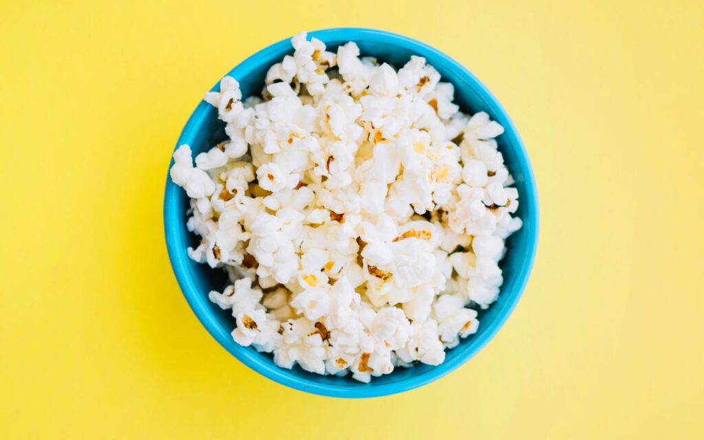 Bowl of freshly popped popcorn in a bright blue bowl on a yellow background
