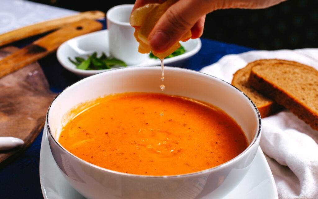 Bowl of red lentil squash soup with lemon juice being squeezed in