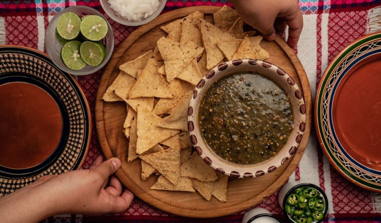 A Person Holding a Wooden Plate with Nachos and Salsa