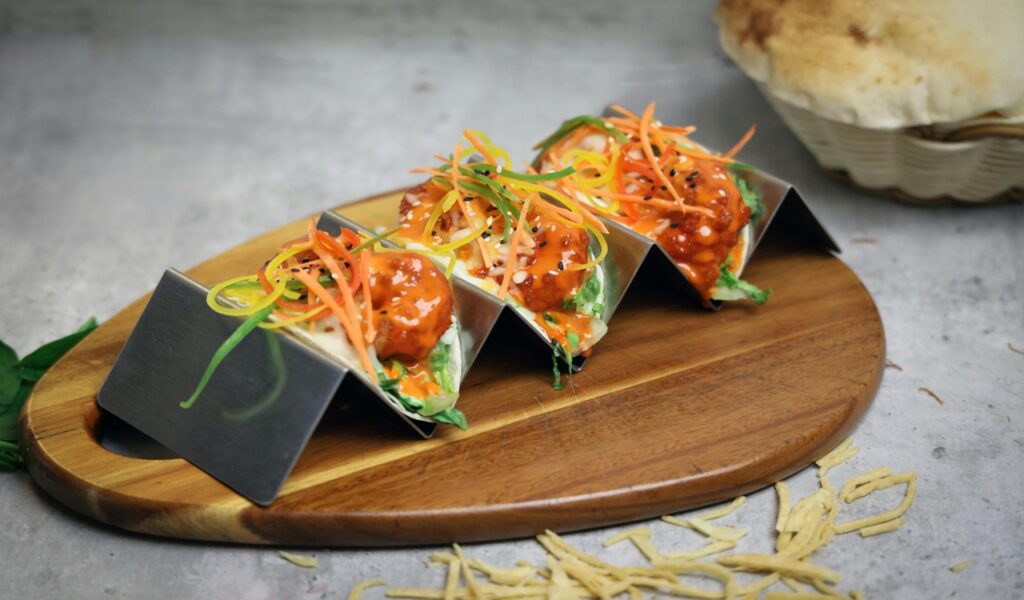 Three tacos on a wooden cutting board with vegetables