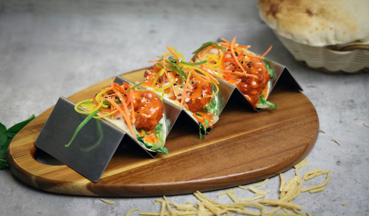 Three tacos on a wooden cutting board with vegetables
