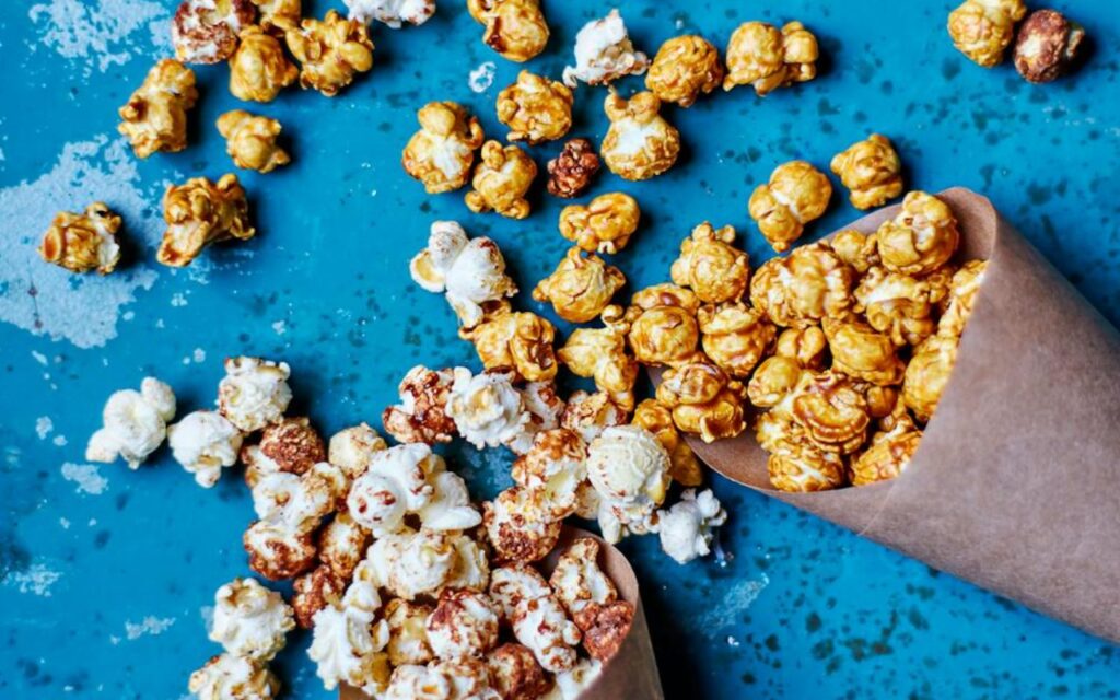 Caramel and cinnamon popcorn in paper cones on blue surface