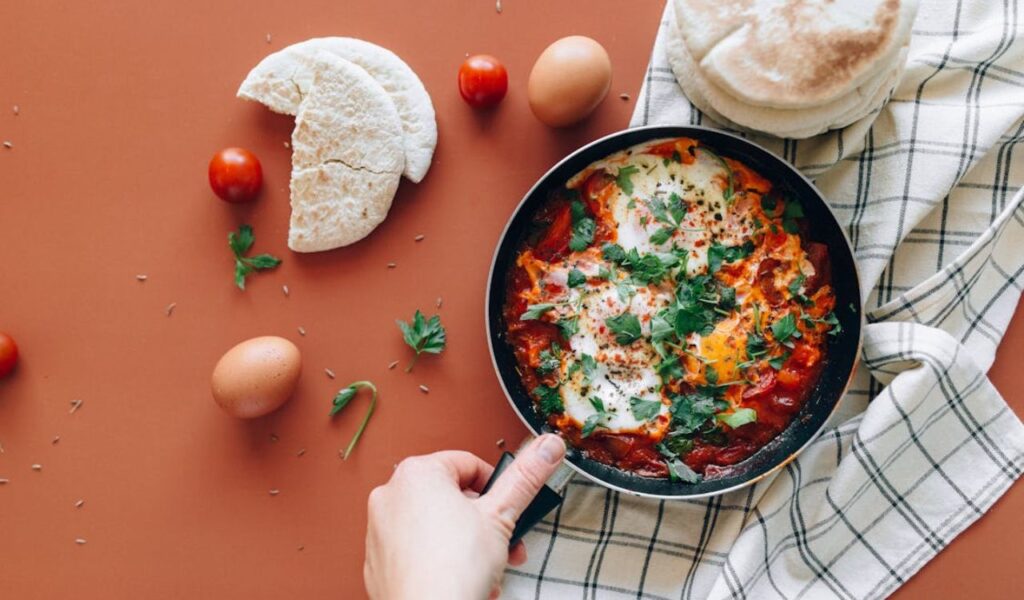 Person Holding a Black Ceramic Pan with Shakshuka