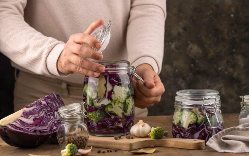 Person sealing a jar of cabbage and broccoli for fermentation