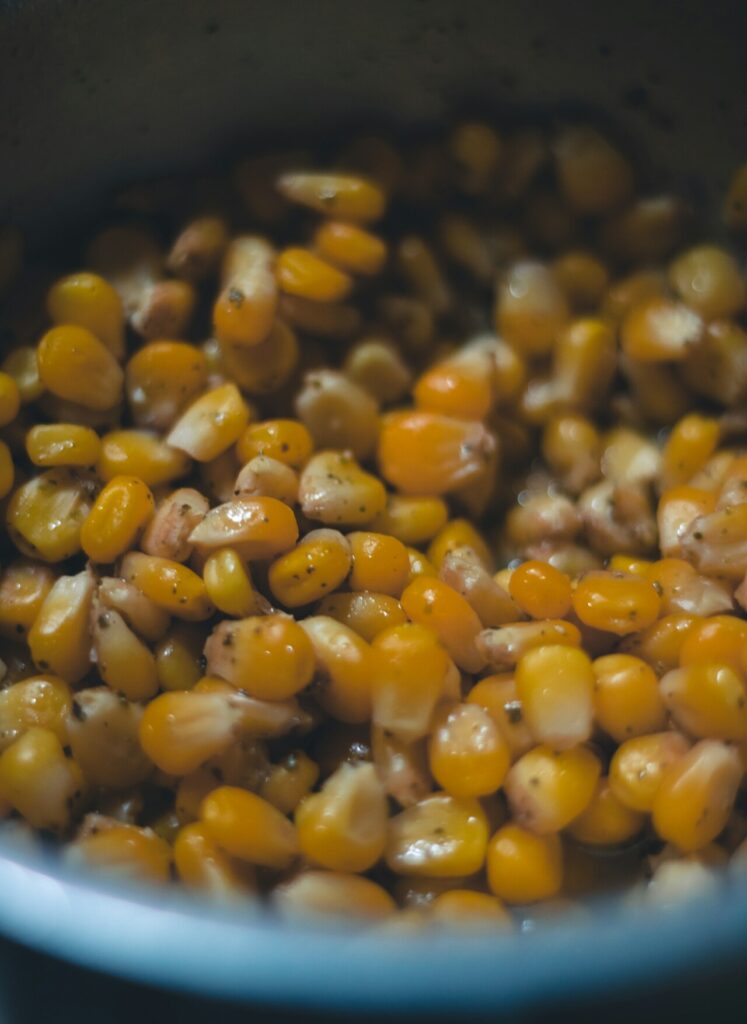 Sautéed corn kernels in a skillet with flecks of green herbs.
