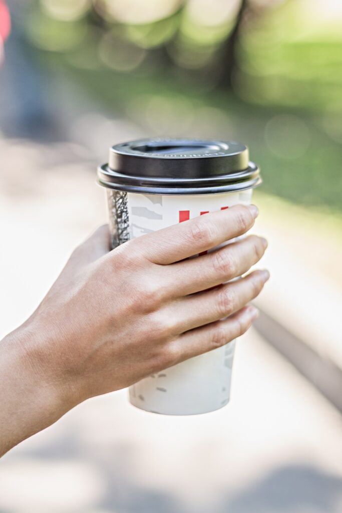 Hand carrying a to-go coffee cup down a busy sidewalk.

