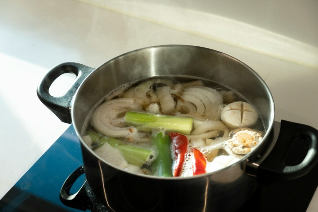 A stockpot simmering on a stove with bones, herbs, and vegetables.