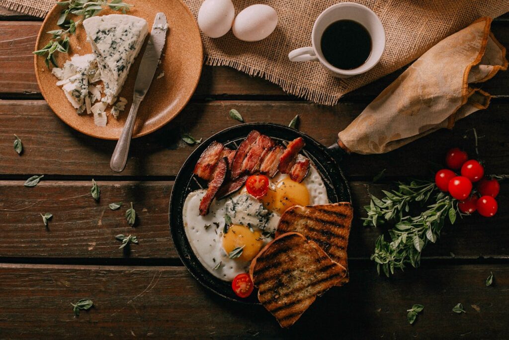 Rustic breakfast table with cast iron pans, a jar of bacon grease, and plates of classic fare.