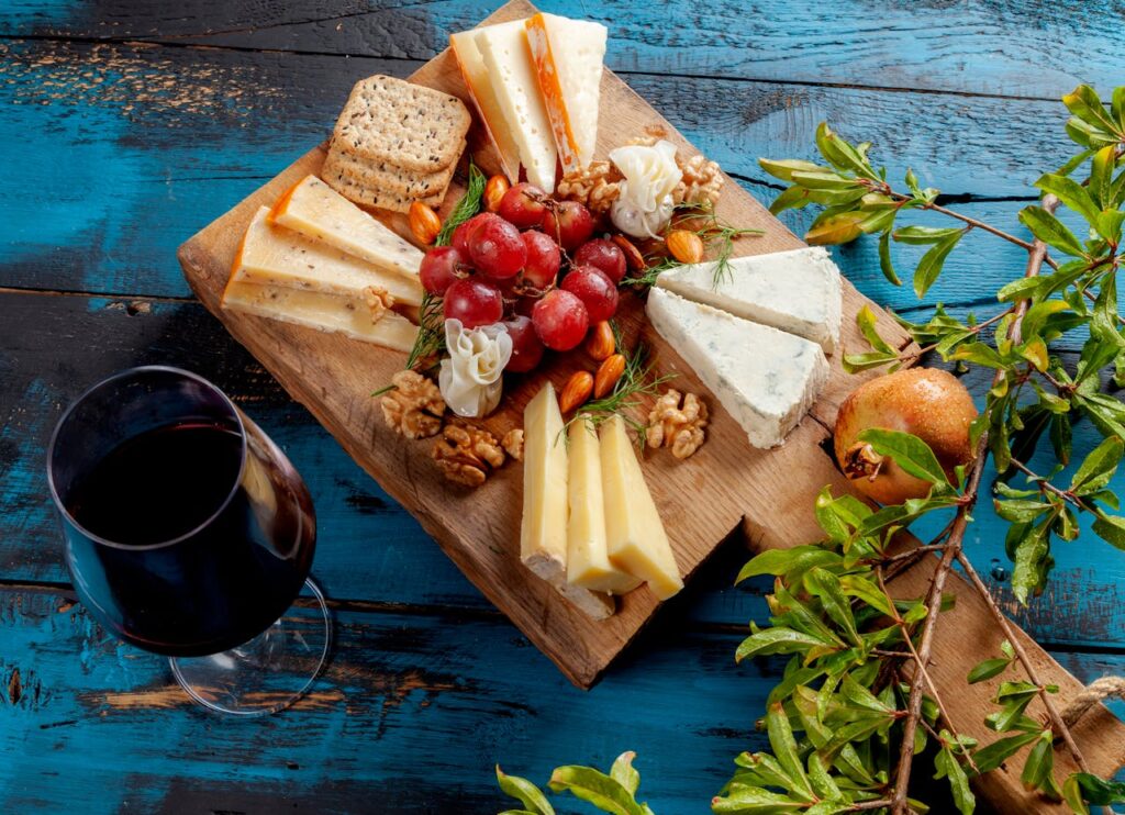 An assortment of French cheeses arranged beautifully on a rustic wooden board with grapes and a glass of wine.