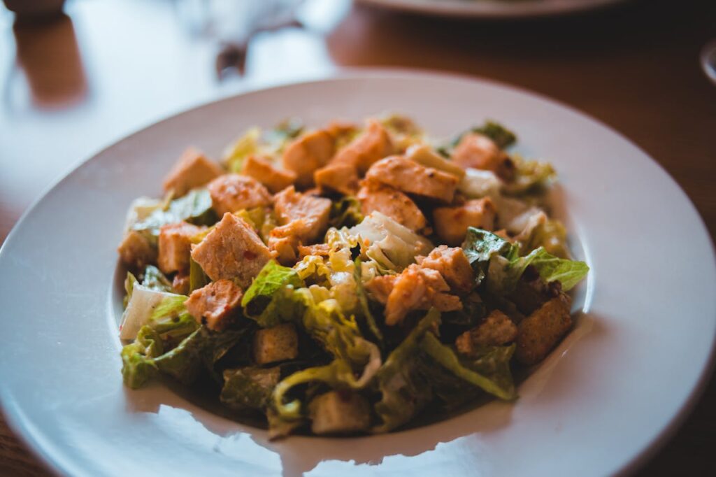 Plated chicken chunks in  salad with fresh vegetables.