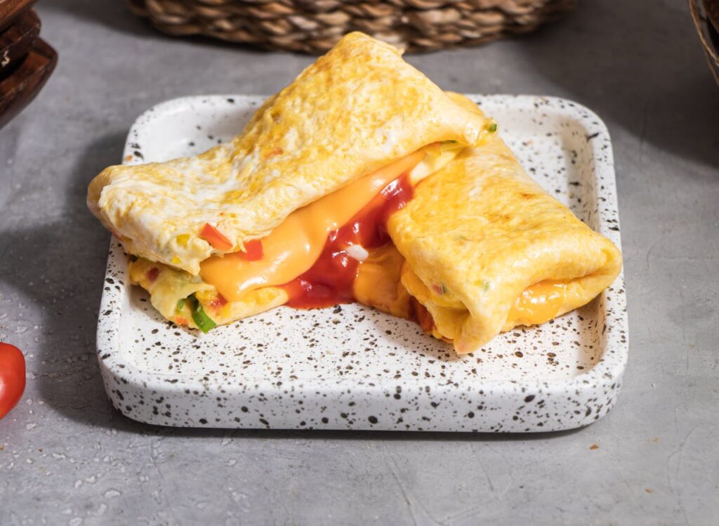 A fluffy omelet folded over sautéed peppers, spinach, and melted cheese on a white plate.