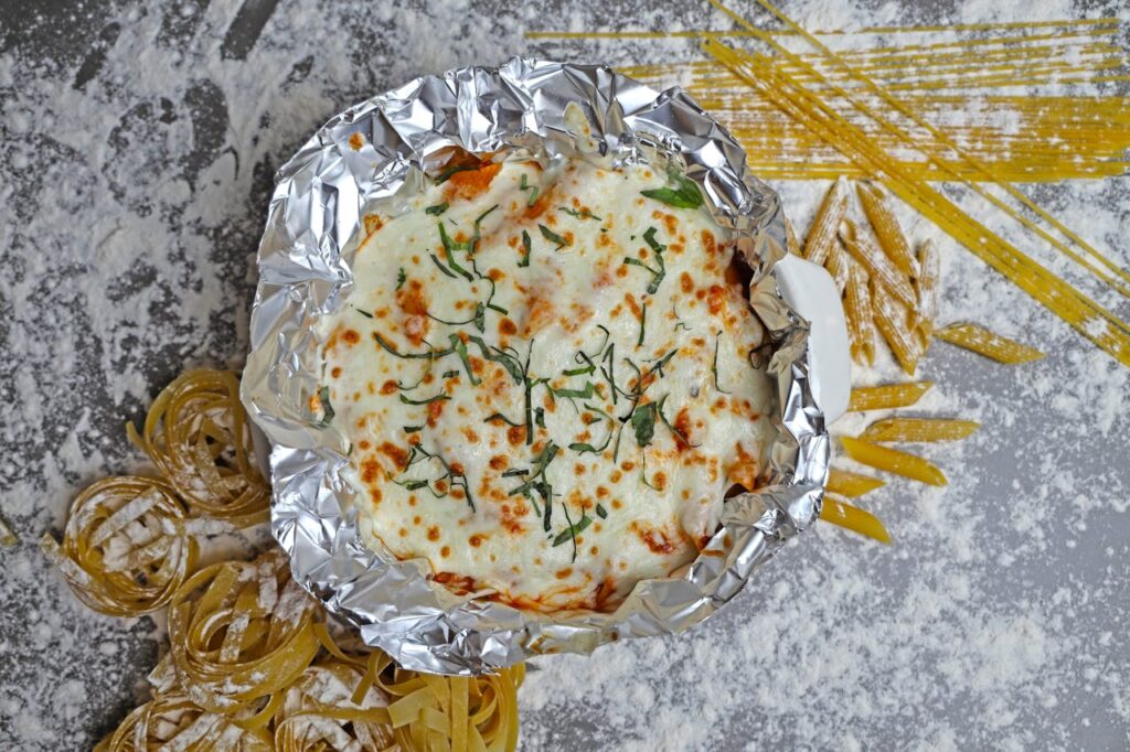 A foil pan with pasta and cheese on top