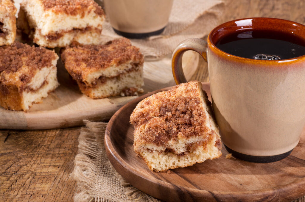 Piece of cinnamon swirl crumb cake and cup of coffee on a wooden plate