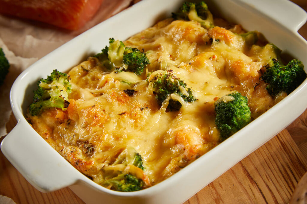 A cheesy vegetable casserole being served with visible chunks of broccoli, peppers, and mushrooms.