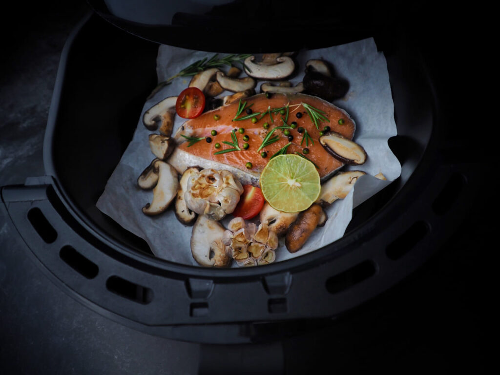 Fresh Salmon fillet with thyme, garlic and lemon slices,shiitake mushroom tomatoes in air-fryer.clean and healthy food in dark tone.