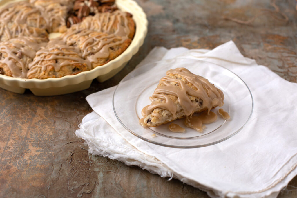 Homemade Pecan Scones on a Rustic Background; One on a Plate in Front and Plate of Scones in Background