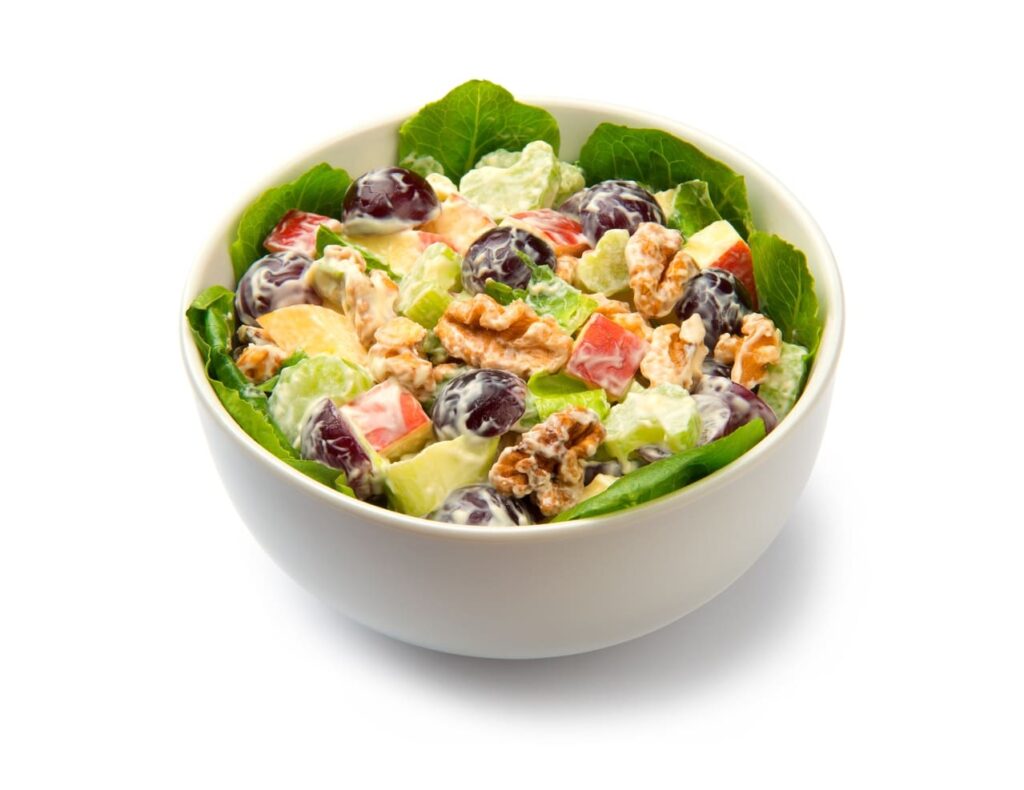 Waldorf salad of apples, celery stalks, walnuts, grapes, lettuce in a white salad bowl isolated on white background.