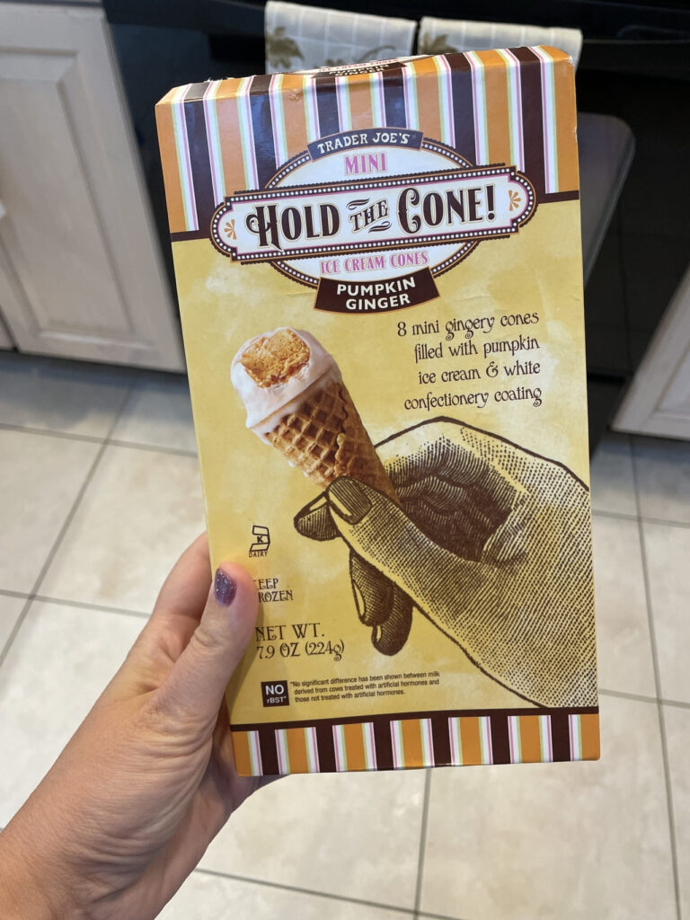 The close up view of a woman holding a box of Trader Joe's Mini Hold the Cone! ice cream cones in pumpkin ginger flavor in a kitchen.
