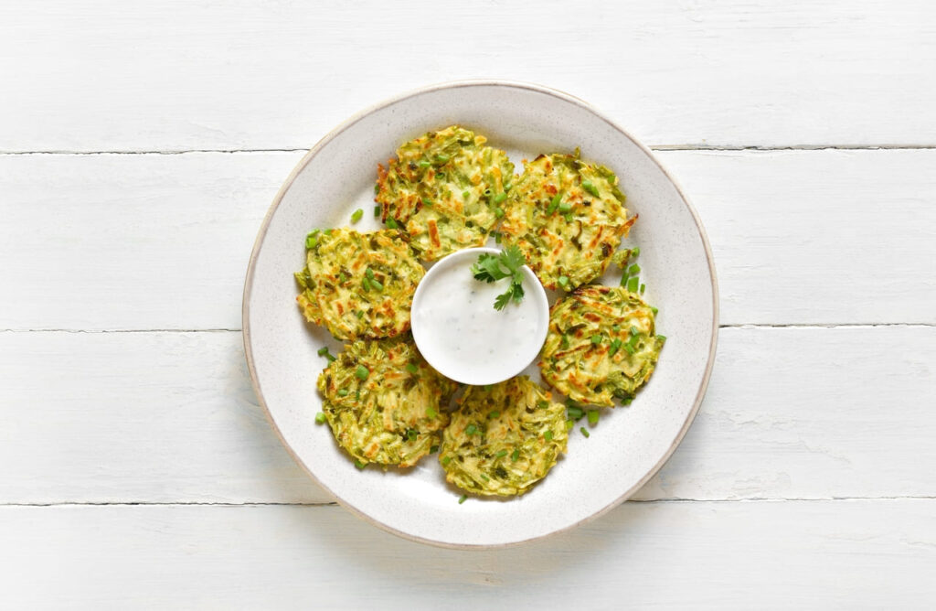 Vegetable vegetarian zucchini fritters pancakes on plate over white wooden background. Top view, flat lay
