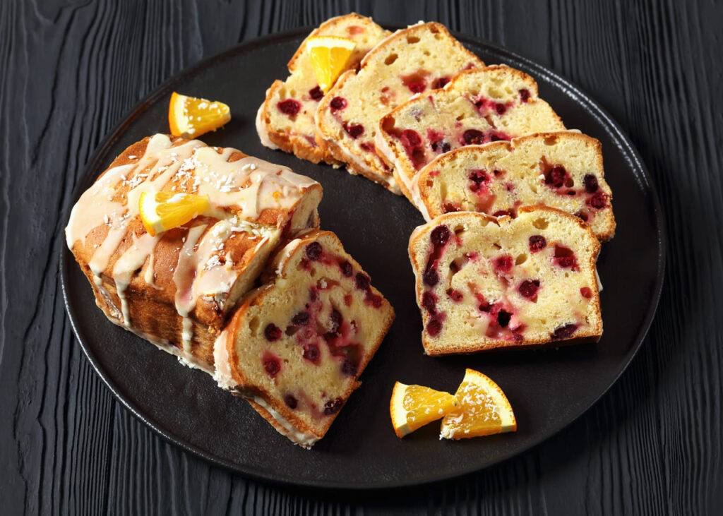 Cranberry orange loaf sliced with fresh cranberries and orange zest nearby