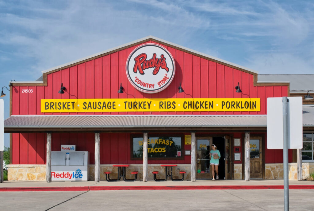 Rudy's Country Store and Bar-B-Q restaurant storefront exterior customer exiting, Reddy Ice freezer Houston TX USA.
