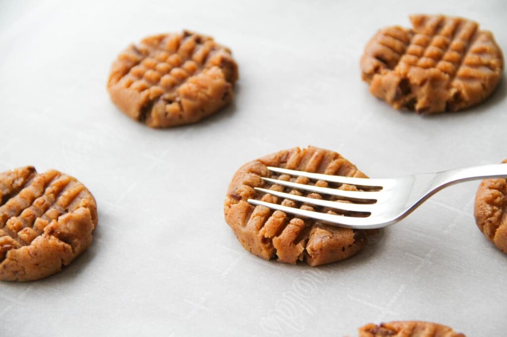 Process of making peanut butter cookies. The cookie dough is pressed with a fork to make a traditional pattern.