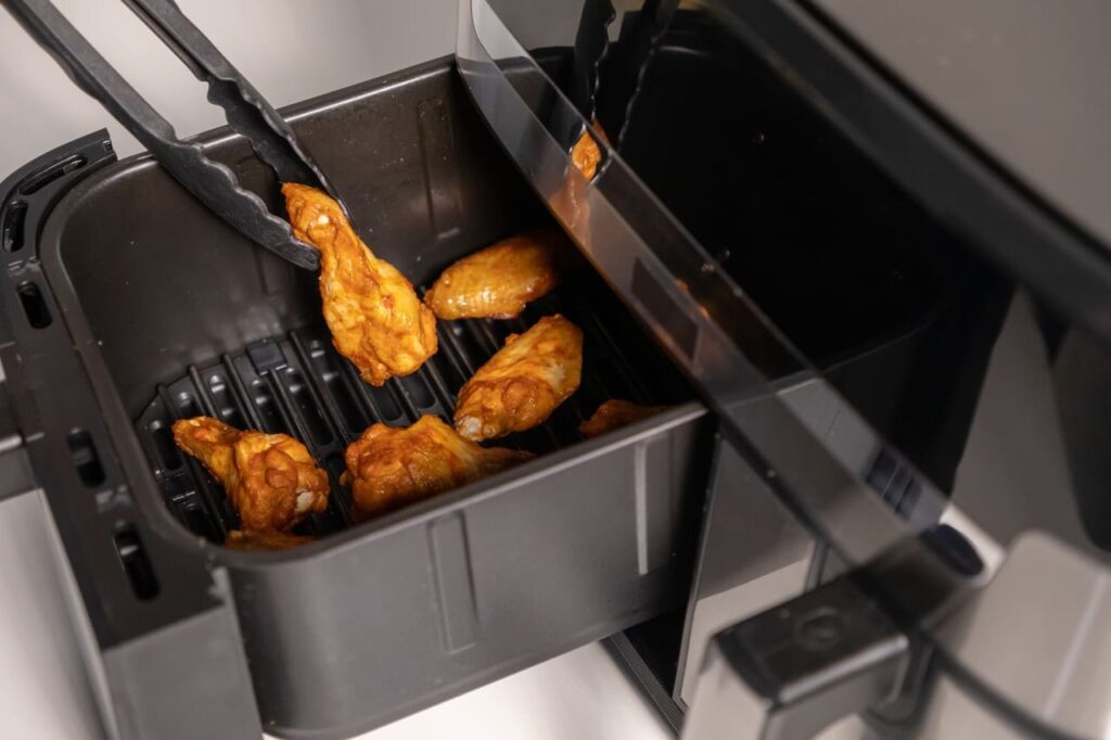 Chicken wings in air fryer being lifted with tongs, golden and crispy after cooking