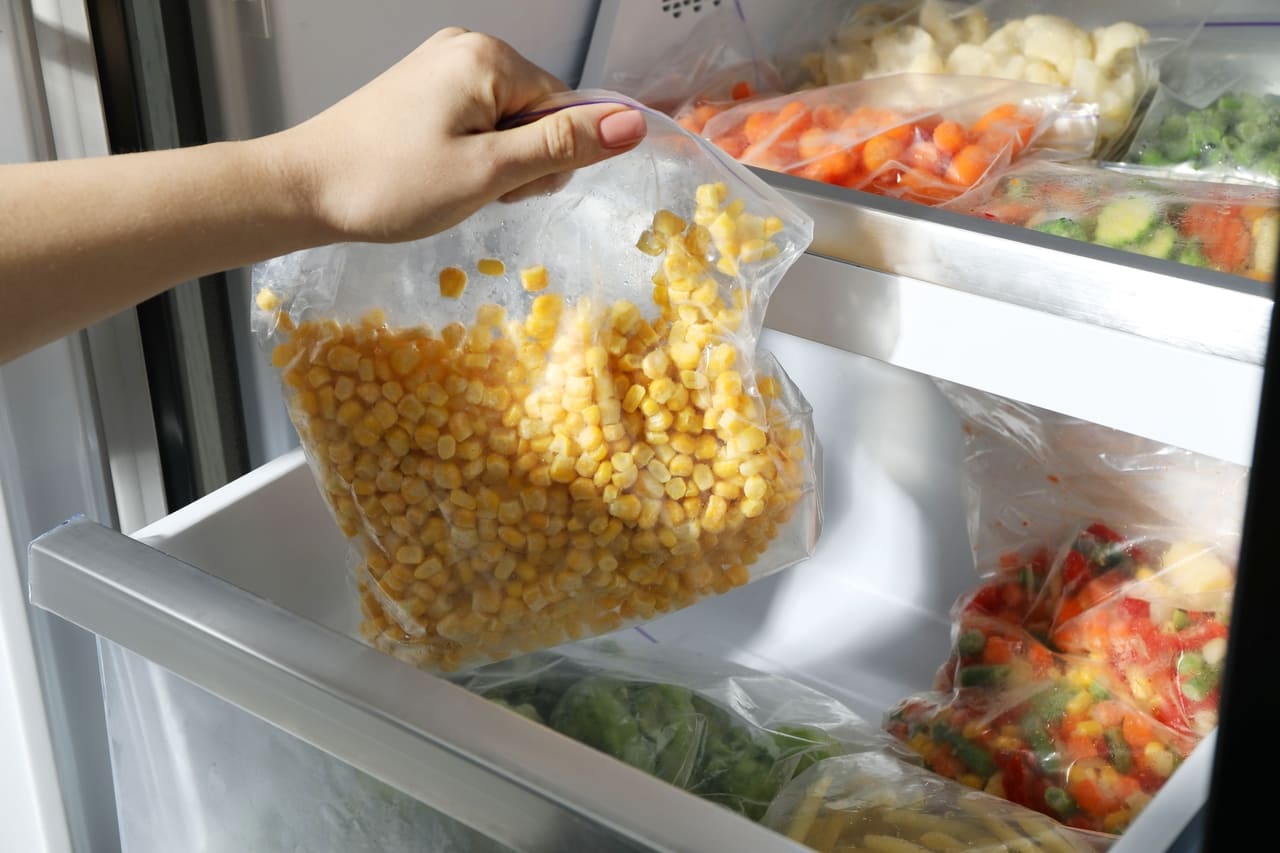 Woman taking plastic bag with frozen corn kernels from refrigerator, closeup