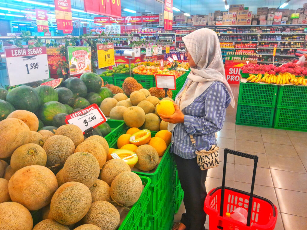 Shoppers holding two cantaloupes and comparing weight.