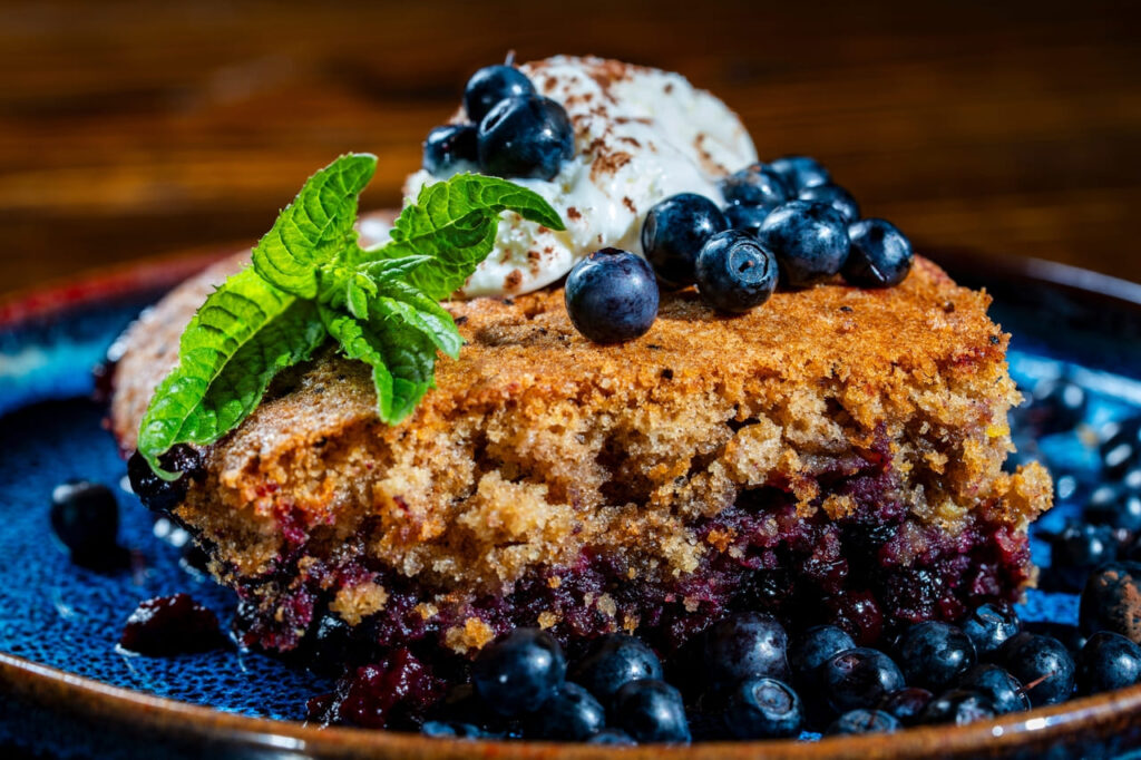 Plate with piece of fresh baked blueberry cobbler and ice cream on wooden background, close up. Homemade berry cobbler ready to eat